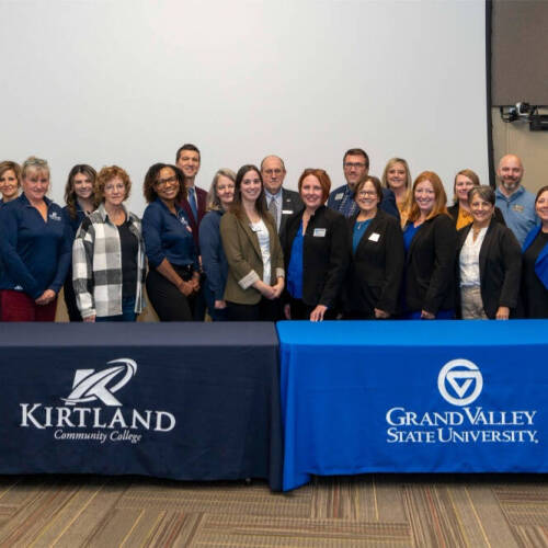 Kirtland Community College and Grand Valley State University standing behind two tables side by side